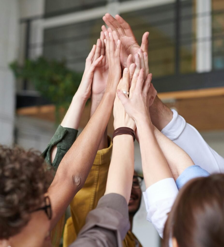 A group of diverse professionals celebrating teamwork with a high-five indoors.